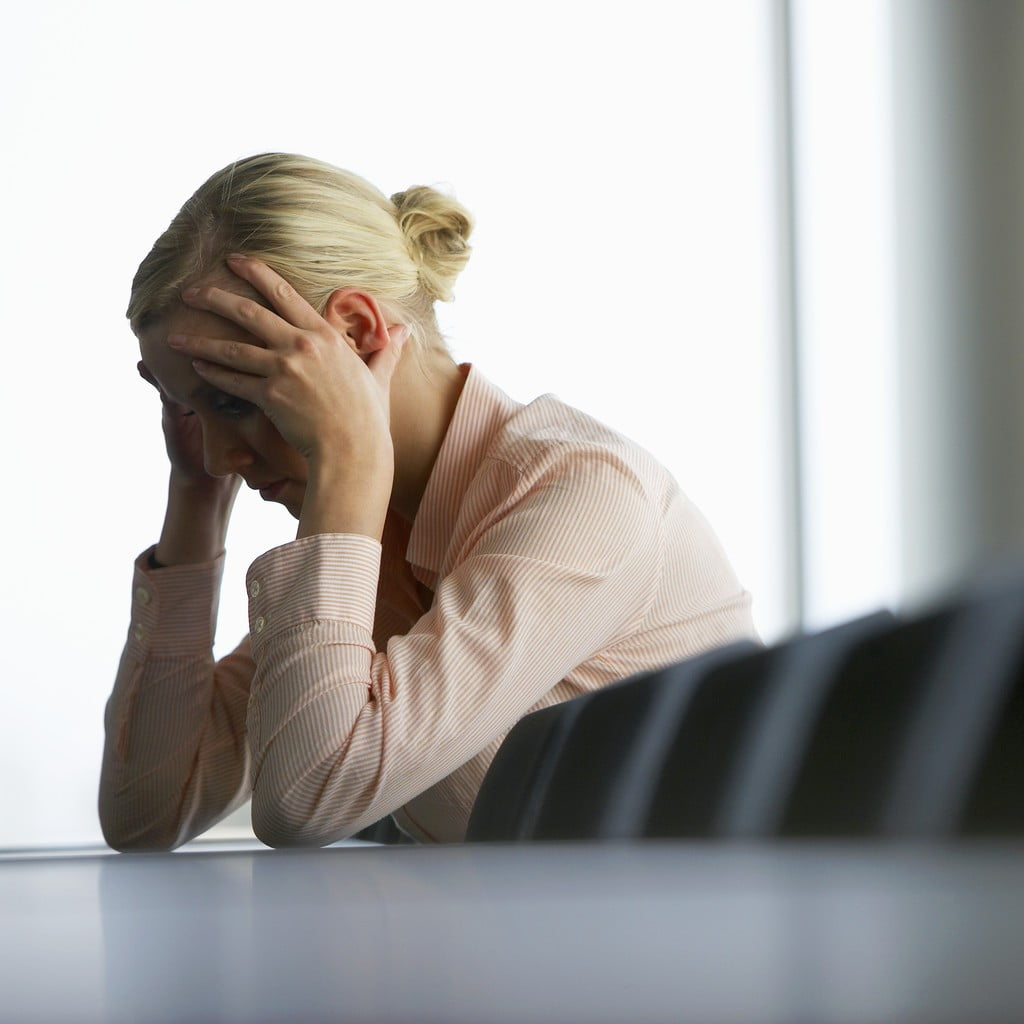Depression - Woman has hands over face lowered on desk